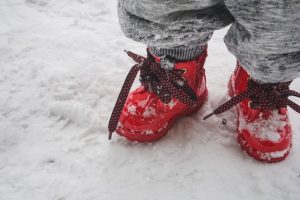 small child's feet in red snow boots standing on snow